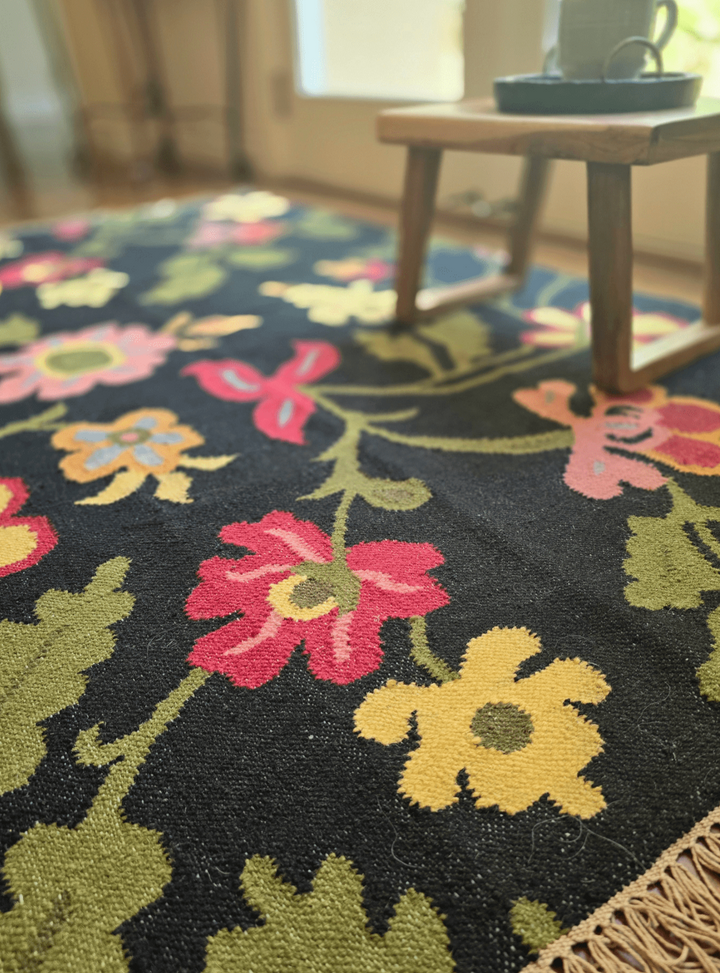 Floral patterned rug with colorful flowers on a dark background, placed in a room.