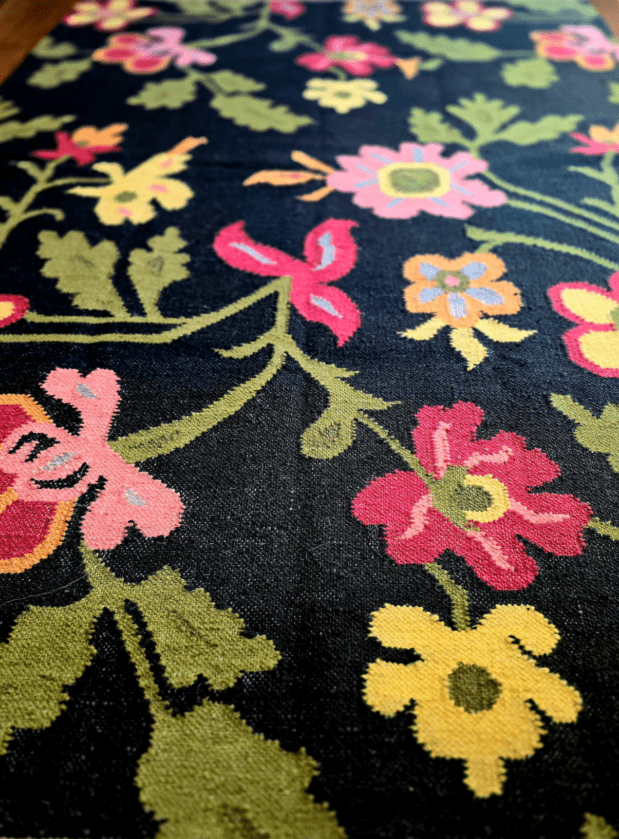Floral patterned rug with colorful flowers on a dark background, placed in a room.