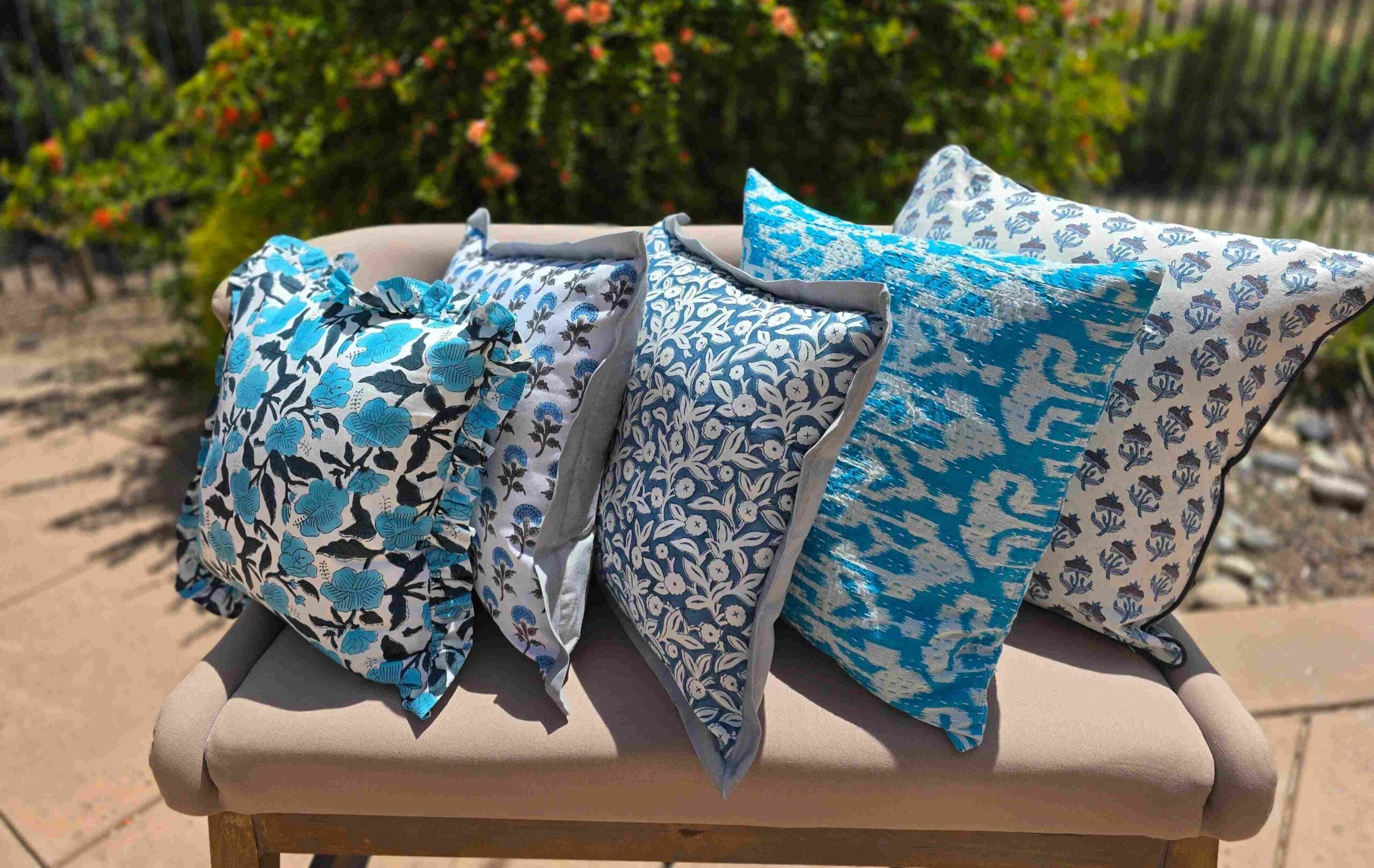 Four floral-patterned pillows on a bench outdoors with greenery in the background