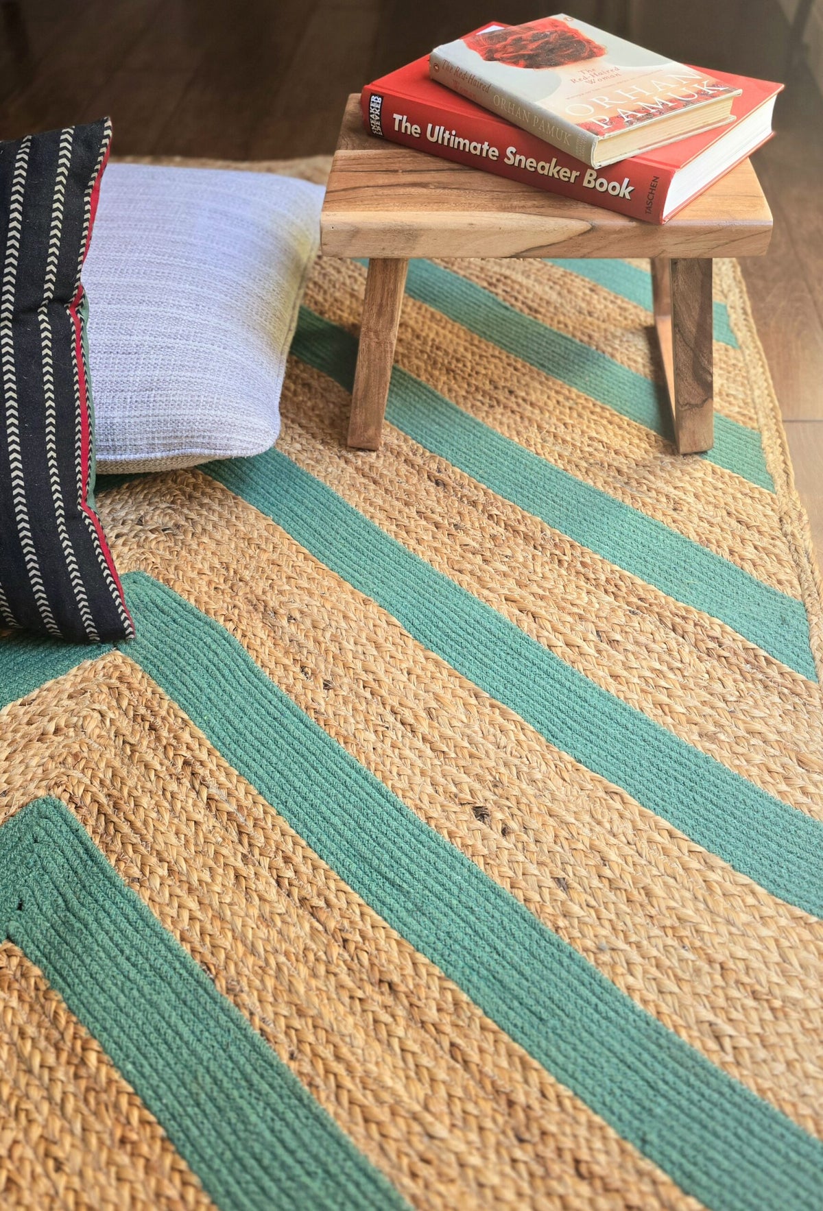 Striped jute rug with a wooden stool and books on a wooden floor.