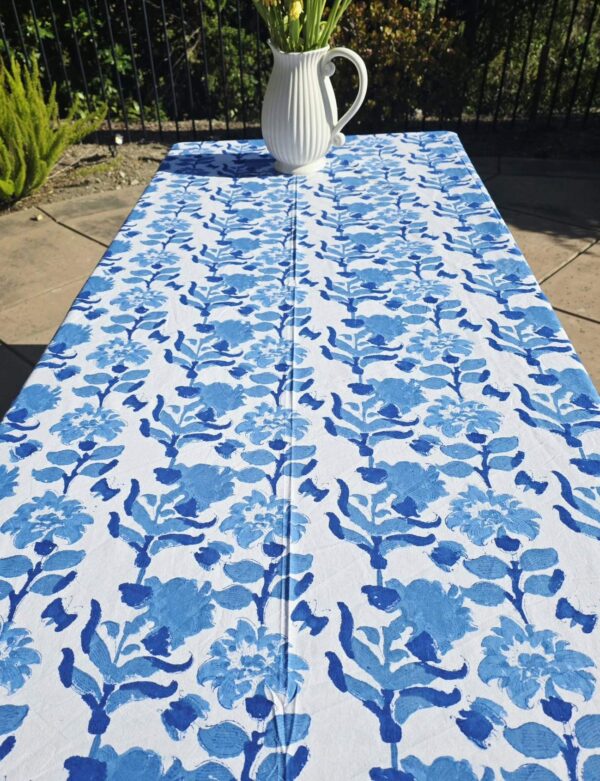 Blue floral cotton tablecloth styled outdoors with flowers and sunlight.