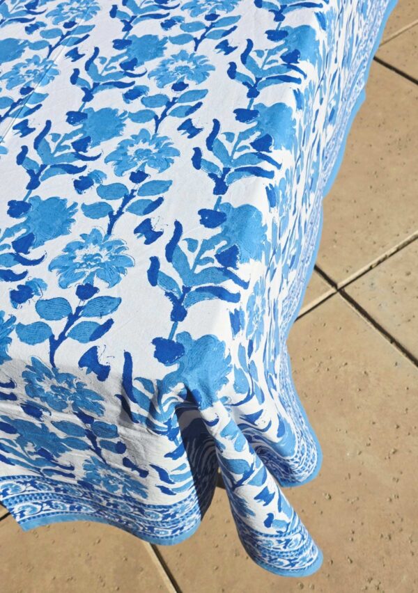 Blue floral cotton tablecloth styled outdoors with flowers and sunlight.