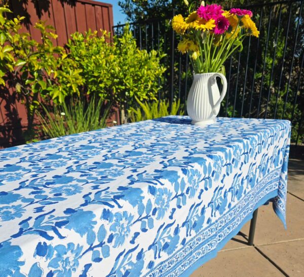 Blue floral cotton tablecloth styled outdoors with flowers and sunlight.