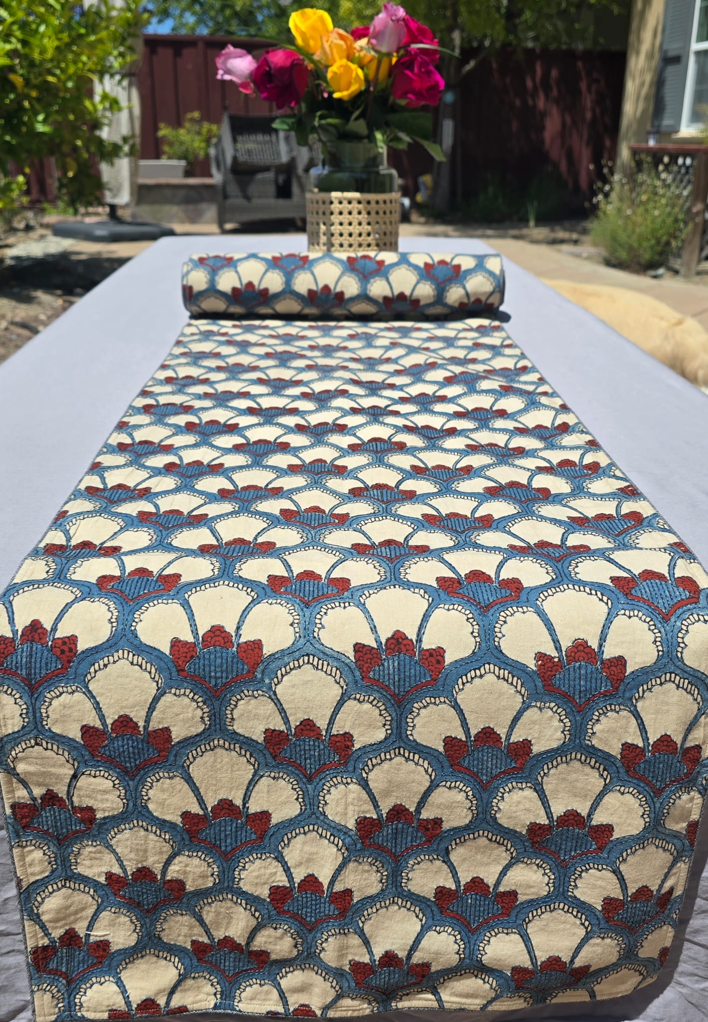 Hand block printed multicolor embroidered cotton table runner on outdoor dining table with floral centerpiece